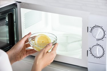 Woman putting bowl with lemon in microwave