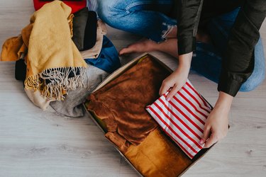 Woman sitting on the floor, folding and packing old used clothes into cardboard donation box.