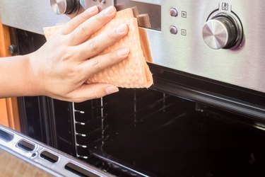 Cropped Hands Of Woman Cleaning Oven At Home