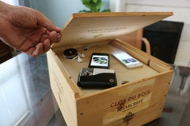 Image of a hand lifting the lid to a wooden box, revealing a DIY charging station filled with devices.