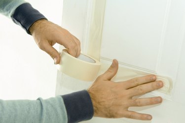 Man putting masking tape on door woodwork, close-up of hands