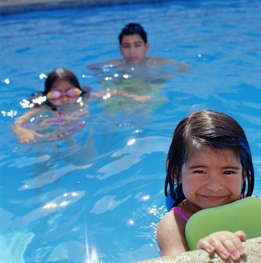 Boy (12-14) and two girls (4-7) swimming in pool (selective focus)