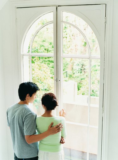 Young Couple Stand Looking Through French Windows Into Garden