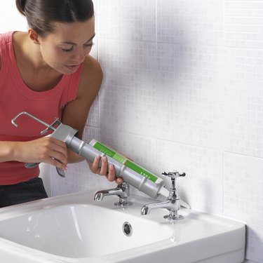 Woman applying sealant between a wall and a sink