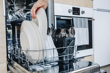 Woman loading the dishwasher. Open dishwasher with clean glasses and dishes close-up after washing.