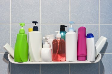 Many shampoo and soap bottles on a bathroom shelf.