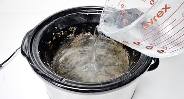 Cleaning out stubborn mess inside slow cooker with water and vinegar.