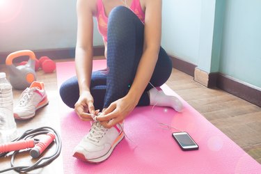 Low Section Of Woman Tying Shoelace While Sitting On Exercise Mat At Home