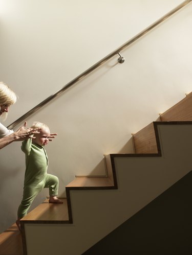 Mother helping baby boy walk up stairs