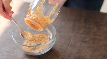 Sprinkling graham cracker crumbs onto drips of caramel sauce on jar.