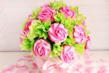 Rose cupcake bouquet against a pale pink background, with a scattering of rose petals underneath.