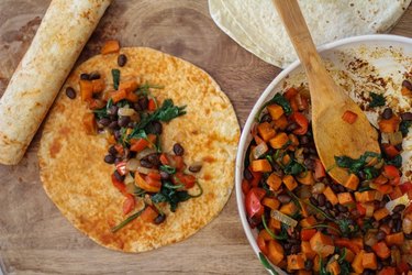 Tortilla with vegetable filling on top next to the skillet of sauteed vegetables.